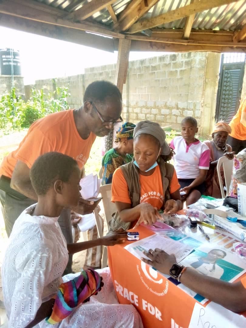 A volunteer health worker in an orange shirt taking a community member's vitals during a one-on-one consultation at the outreach.